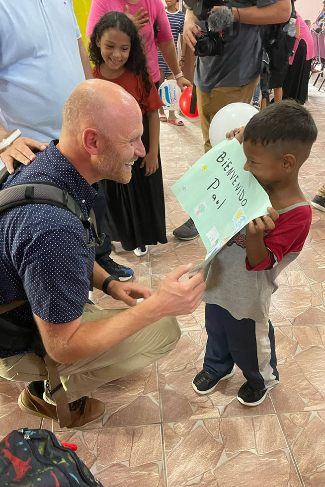 CCU campus pastor Paul Faust smiles as he bends down to read a handmade art project shown by a Honduran child