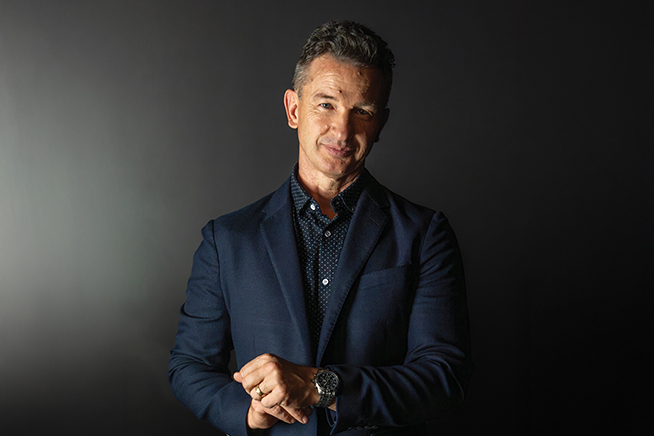 greg stier adjusting his watch wearing a suit against a dark background
