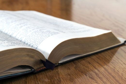 A holy Bible is sitting on a wooden desk.